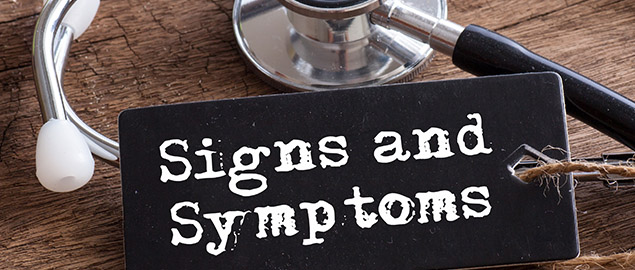 On a wooden desk is a stethoscope and a black sign with “Signs and Symptoms” on it.